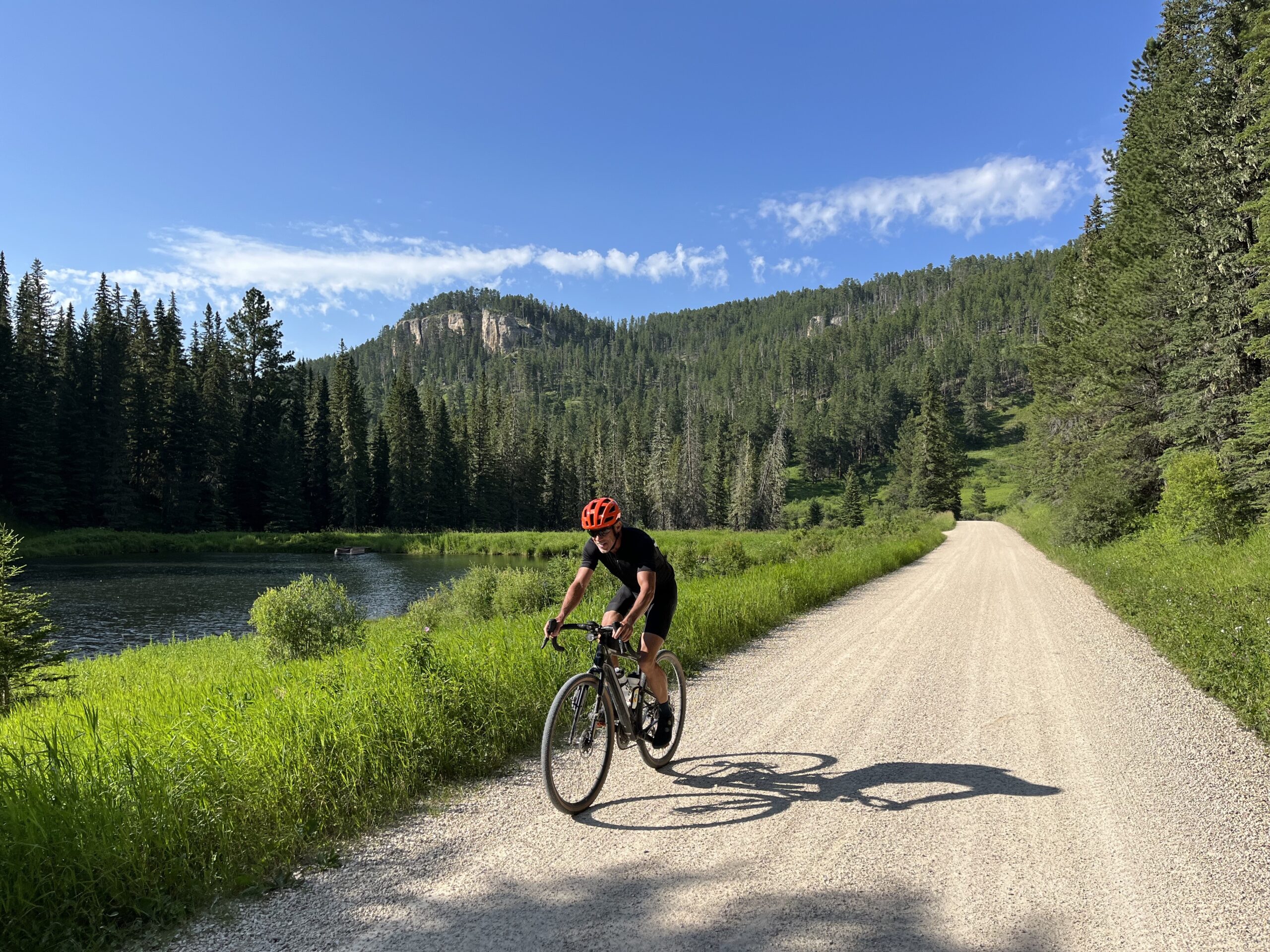 Cyclist on dirt road riding past a lake and mountain
