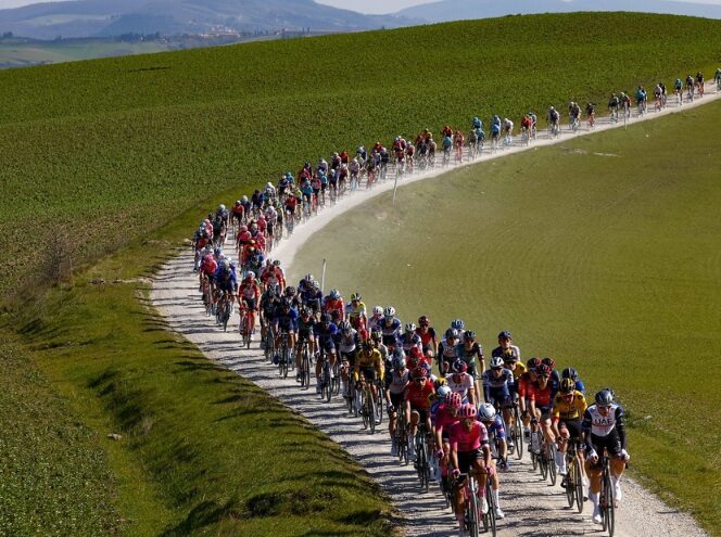 Large peloton riding along the gravel roads of Tuscany with farm fields on either side