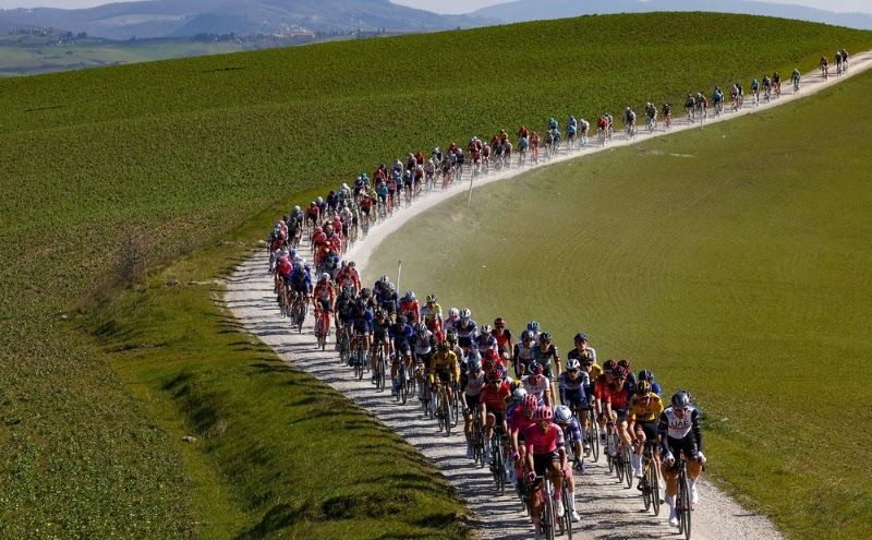 Large peloton riding along the gravel roads of Tuscany with farm fields on either side