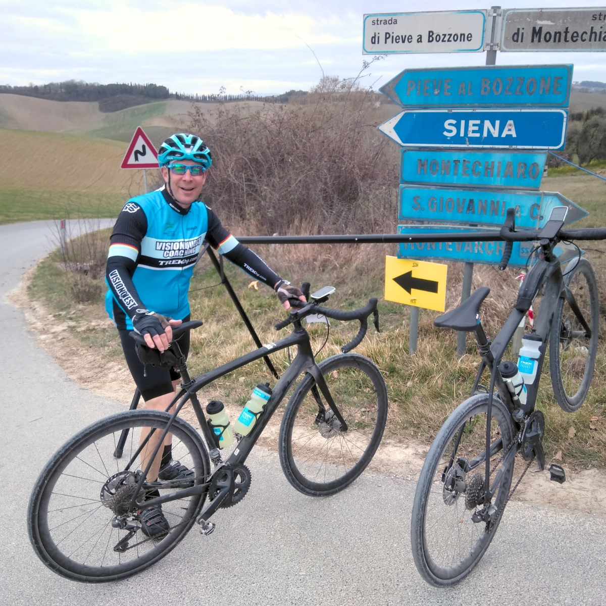 Cyclist with two bicycles and bike rack in front of Siena direction signs