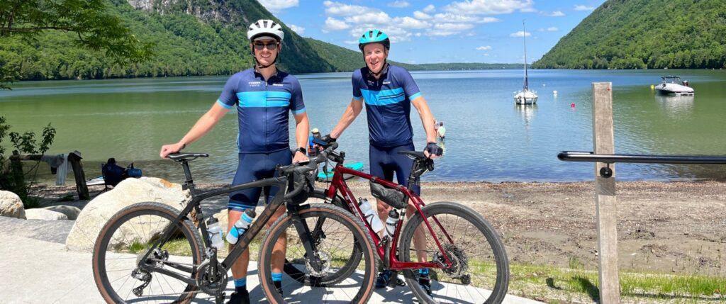 Two cyclists in front of a lake with sailboats