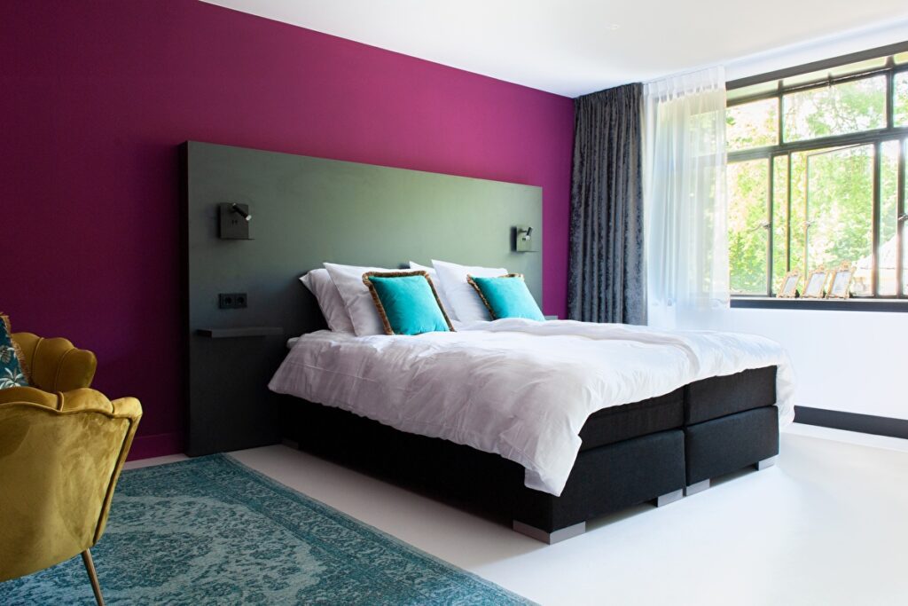Double bed with deep fuscia walls and large window.