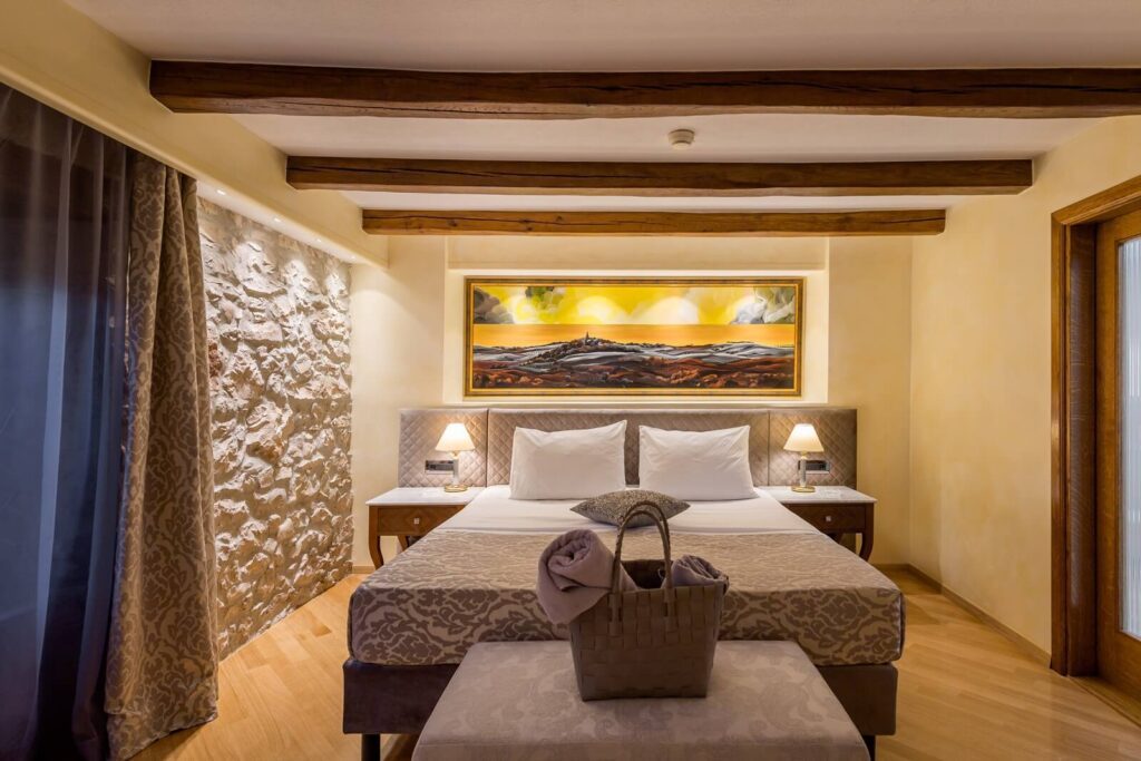 Double bed with painting, wood beam ceiling, and basket at Hotel San Rocco