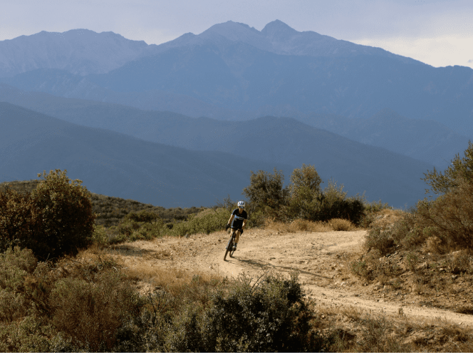 Single cyclist on gravel road with mountains in the background