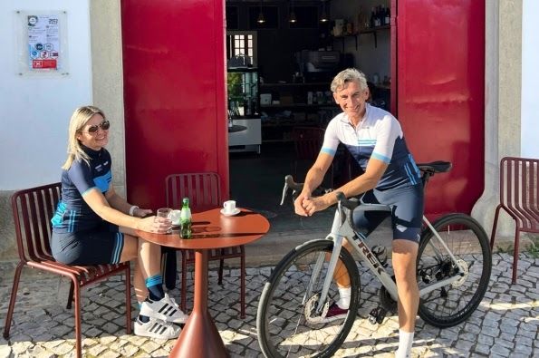 Two people smiling on a terrace with a small table and a bike