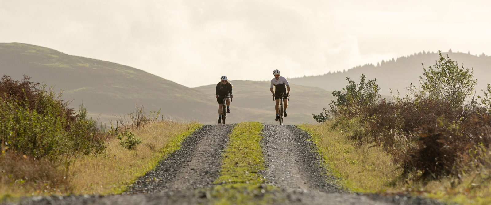 Two cyclists on a gravel roadway with hills in the background