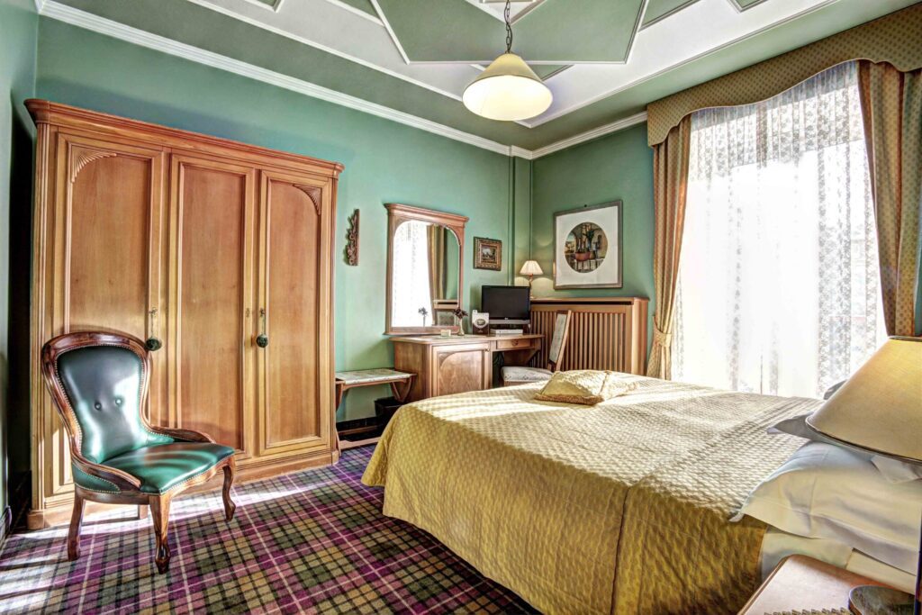 Double bedroom with high-back chair and large wardrobe at Storico Hotel Regina