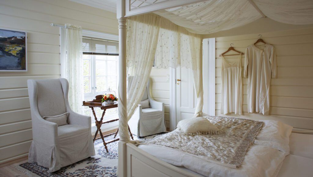 Canopy bed with wood slat walls and arm chairs in a bright room at hotel Bestebakken