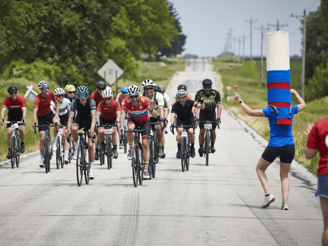 Group of cyclists riding together with cheering person in costume on the side of the road