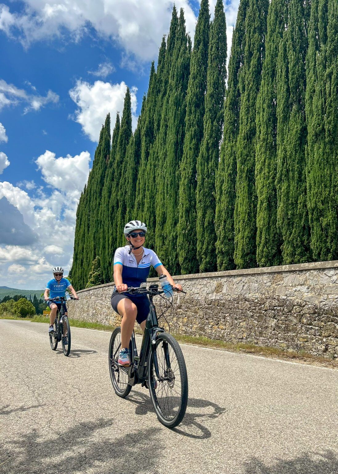 A woman biking in Tuscany along a lane of trees.