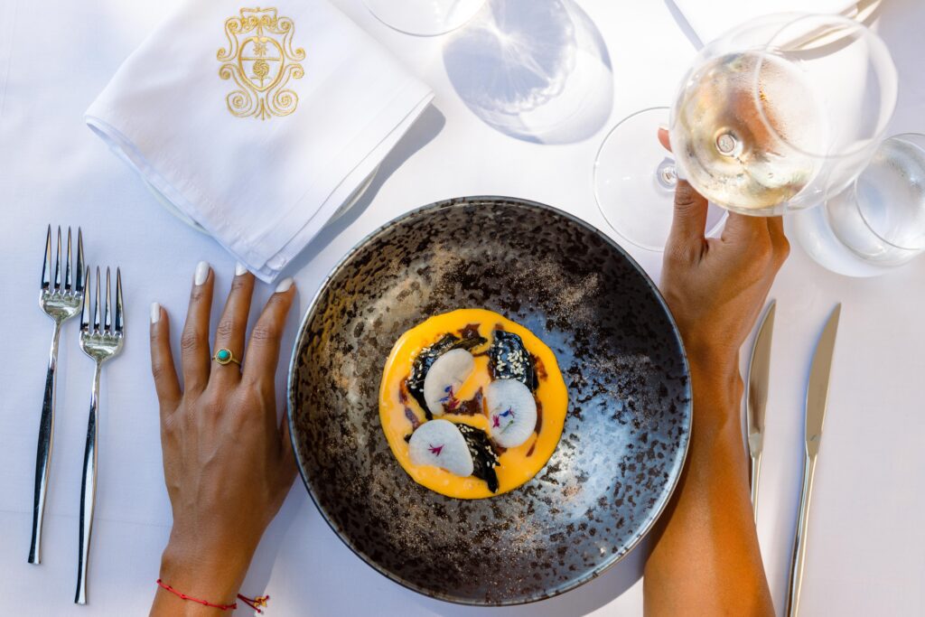 Woman's hands around a decorative plate of food and a glass of white wine.