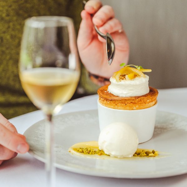 Person eating a lemon souffle dessert and glass of white wine.