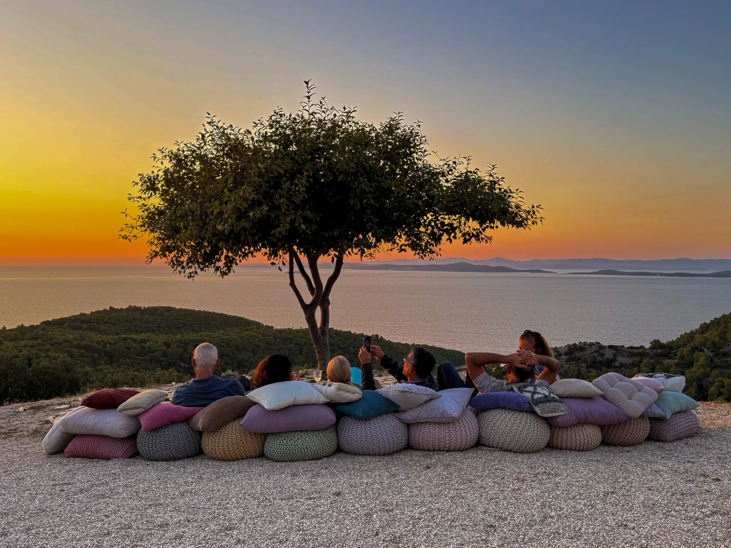 A group of people sitting down staring out at the sunset in Croatia.